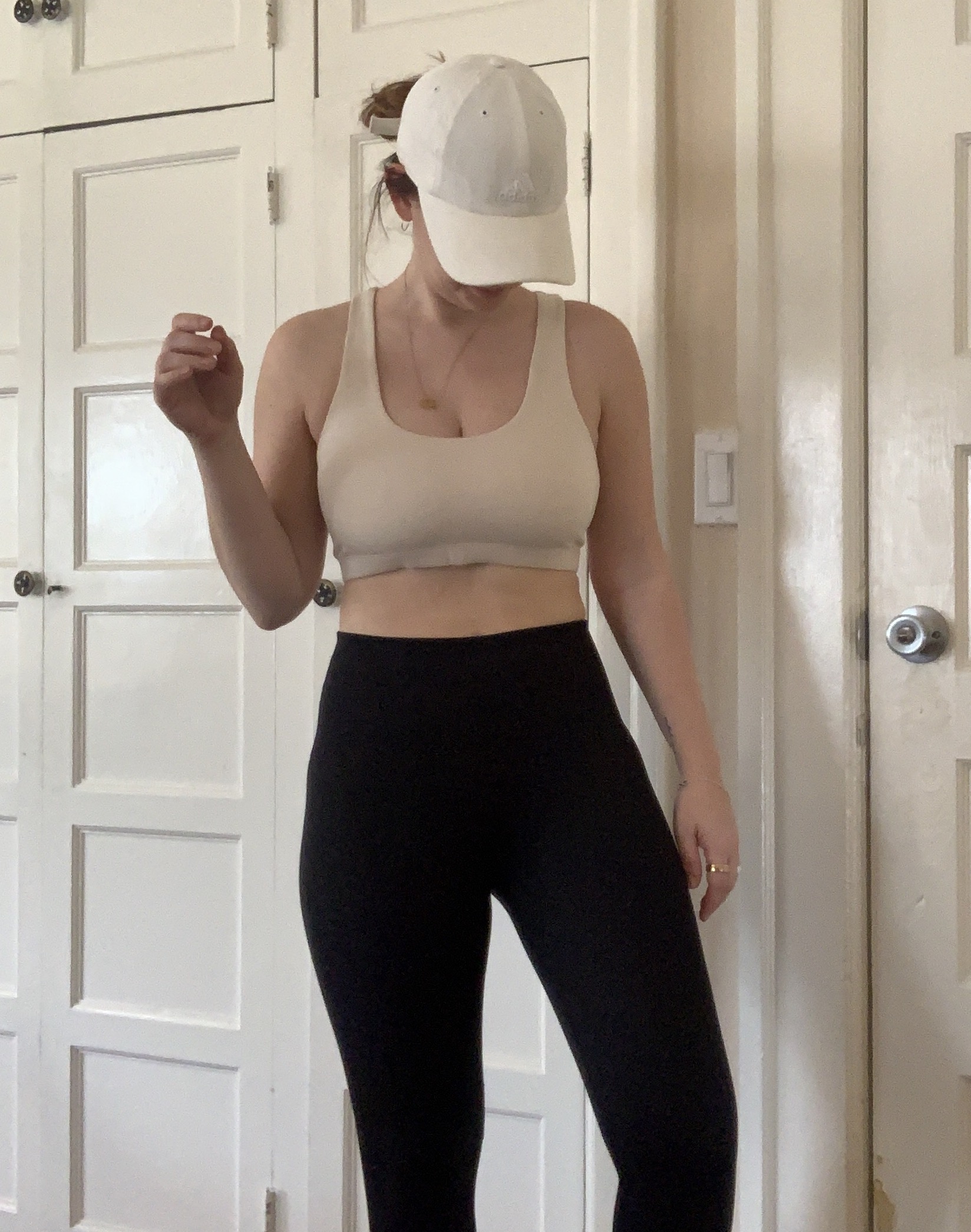 Person wearing a beige crop top, black pants, and a white cap stands in a room with white paneled doors.