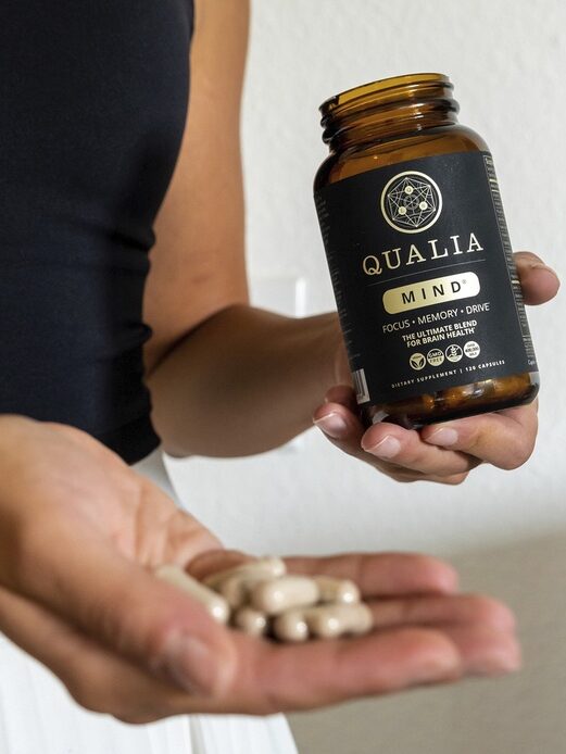 Person holding a bottle of Qualia Mind supplements and showing several capsules in their hand.