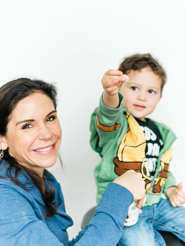 A child seated next to their parent,  holding up Raise Them Well chewable multivitamins.