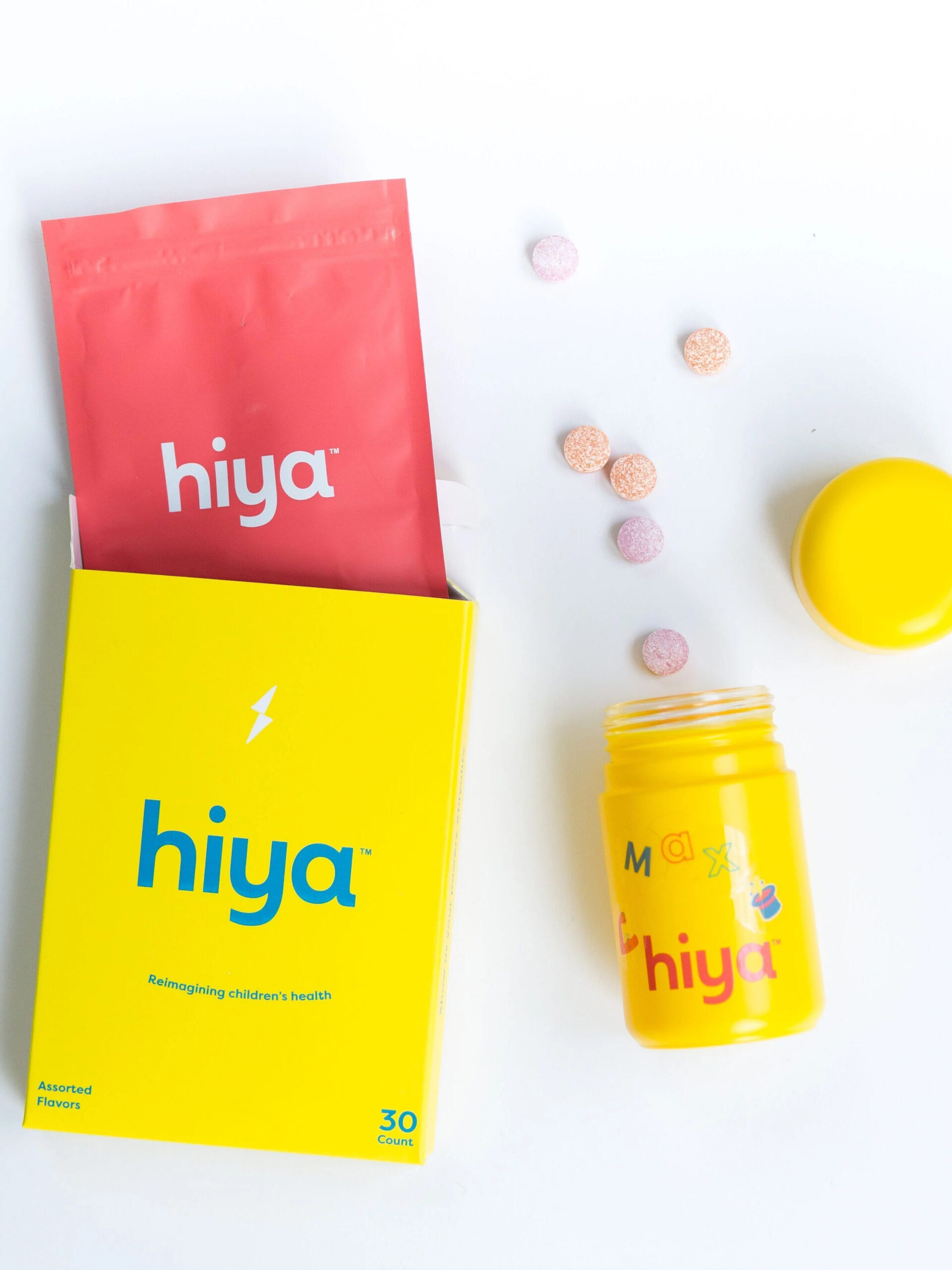 Yellow container labeled "hiya" with multicolored tablets scattered.